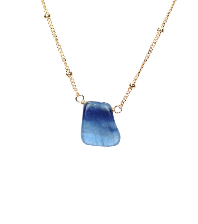 May include: A gold chain necklace with a blue gemstone pendant. The pendant is a freeform shape and has a light blue color.