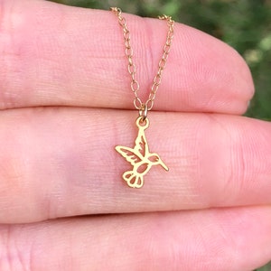 May include: A gold chain necklace with a delicate hummingbird pendant. The hummingbird is cut out of the metal, creating a delicate and airy design.