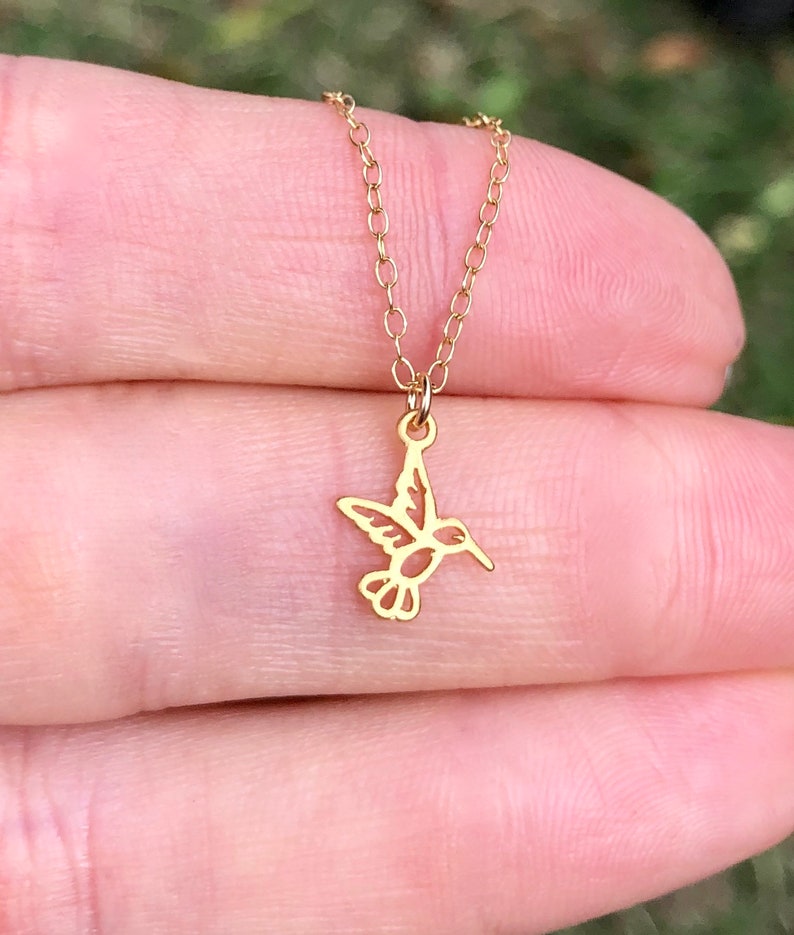 May include: A gold chain necklace with a delicate hummingbird pendant. The hummingbird is cut out of the metal, creating a delicate and airy design.