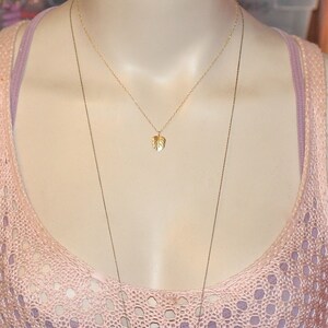 Peut inclure: Un collier en or avec un pendentif d&eacute;licat en forme de feuille. Le collier est superpos&eacute; &agrave; un haut en crochet rose et blanc.