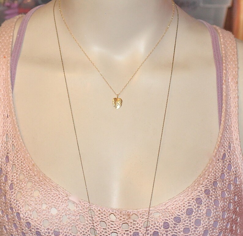 Peut inclure: Un collier en or avec un pendentif d&eacute;licat en forme de feuille. Le collier est superpos&eacute; &agrave; un haut en crochet rose et blanc.