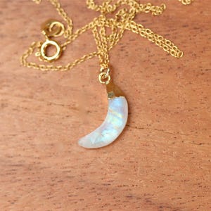 May include: A gold chain necklace with a crescent moon pendant made of iridescent moonstone.