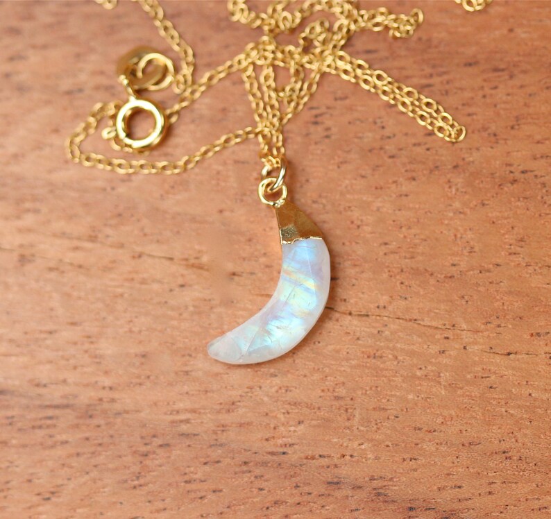 May include: A gold chain necklace with a crescent moon pendant made of iridescent moonstone.