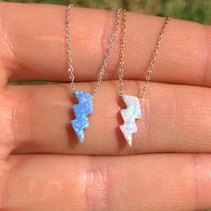 May include: Two silver and gold necklaces with opal lightning bolt pendants. The silver necklace has a blue opal pendant and the gold necklace has a white opal pendant.