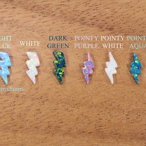 May include: Seven lightning bolt shaped opal cabochons in various colors, including light blue, white, dark green, purple, and aqua. The cabochons are approximately 13mm x 5mm in size.