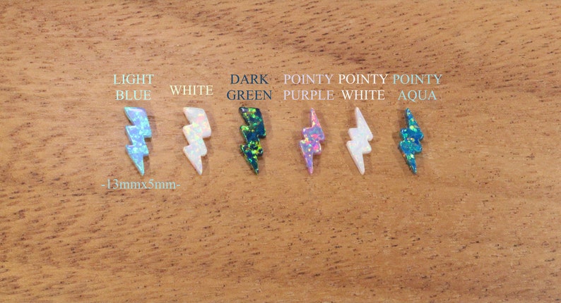 May include: Seven lightning bolt shaped opal cabochons in various colors, including light blue, white, dark green, purple, and aqua. The cabochons are approximately 13mm x 5mm in size.