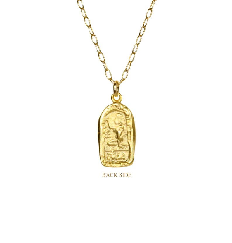 May include: Gold necklace with a pendant featuring an intricate design. The pendant is shaped like a rectangle with rounded corners and has a raised design on the front. The back of the pendant is plain. The necklace is made of a delicate chain.