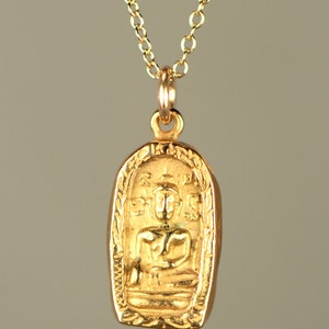 May include: A gold pendant necklace with a small, ornate, rectangular pendant featuring a seated Buddha figure. The pendant has a detailed design with intricate carvings.