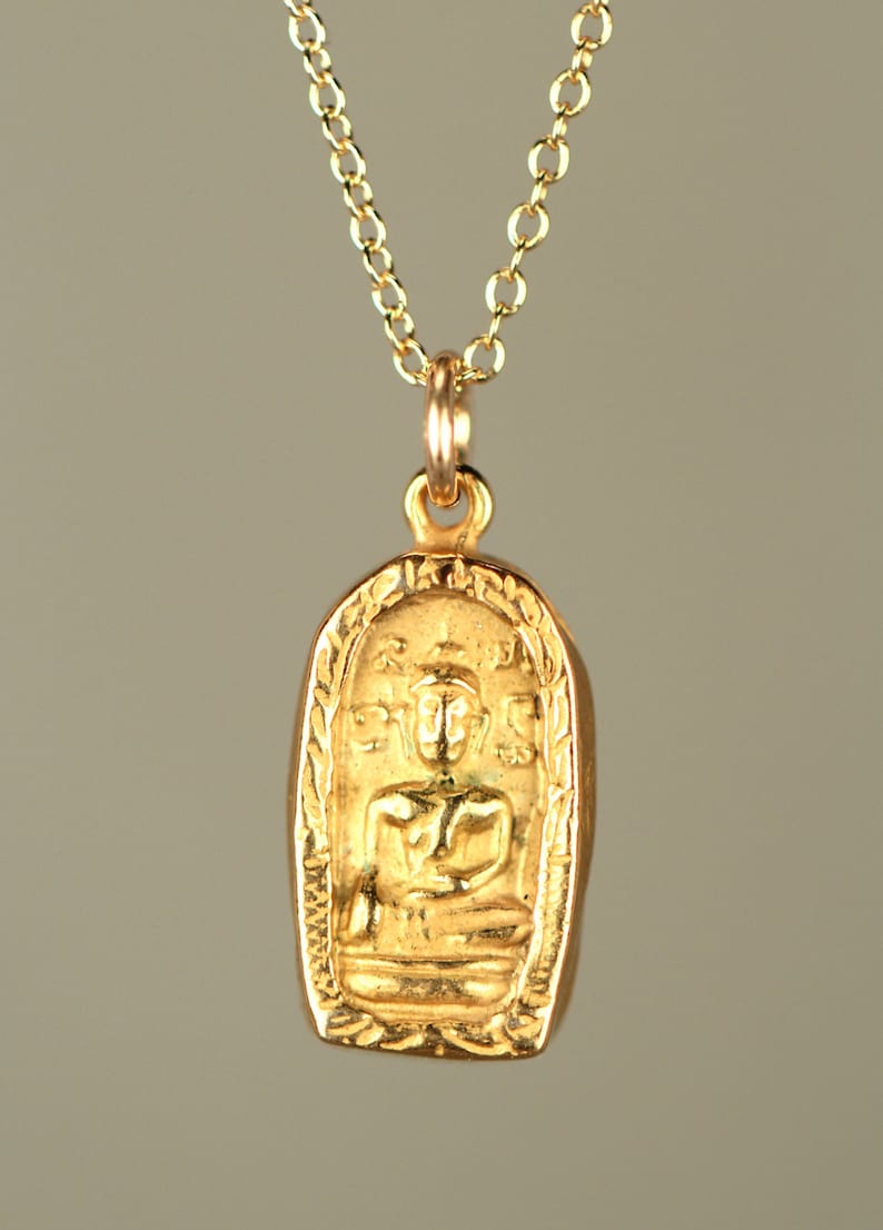 May include: A gold pendant necklace with a small, ornate, rectangular pendant featuring a seated Buddha figure. The pendant has a detailed design with intricate carvings.