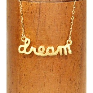 Puede incluir: Un collar de oro con la palabra "Dream" escrita en cursiva.