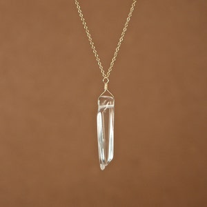 May include: A gold chain necklace with a clear quartz crystal pendant.