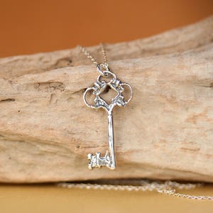 May include: A silver key pendant necklace with an ornate design. The key is on a silver chain.