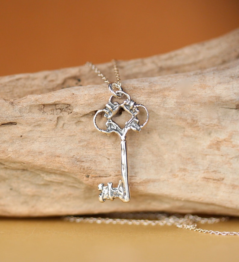 May include: A silver key pendant necklace with an ornate design. The key is on a silver chain.