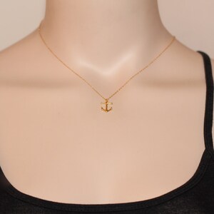 May include: A gold anchor pendant necklace on a gold chain. The necklace is on a mannequin wearing a black tank top.