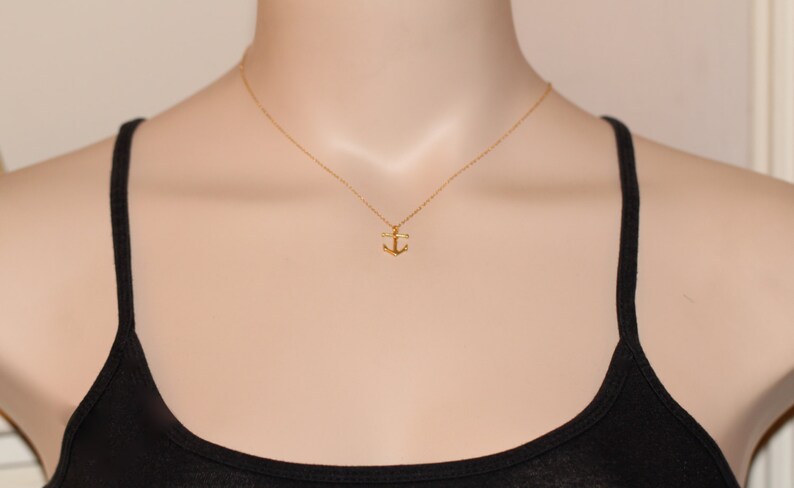 May include: A gold anchor pendant necklace on a gold chain. The necklace is on a mannequin wearing a black tank top.