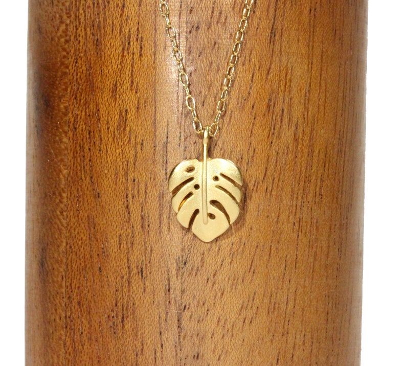Peut inclure: Un collier en or avec une cha&icirc;ne d&eacute;licate et un pendentif en forme de feuille de monstera.