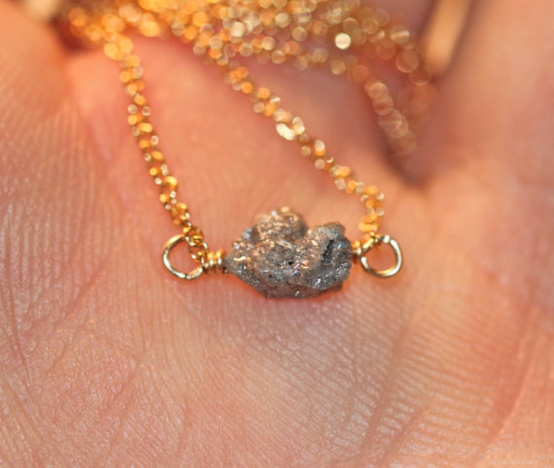 May include: A delicate gold chain necklace with a small, rough, grey diamond pendant.