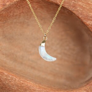 May include: A gold chain necklace with a crescent moon pendant made of iridescent moonstone.