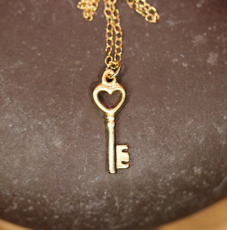 Puede incluir: Un collar de llave de oro con un ojo de cerradura en forma de coraz&oacute;n. La llave est&aacute; en una delicada cadena de oro.