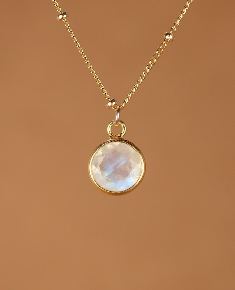 May include: A gold chain necklace with a round, iridescent moonstone pendant.