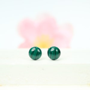 May include: A pair of green malachite stud earrings. The earrings are round and have a smooth, polished finish.