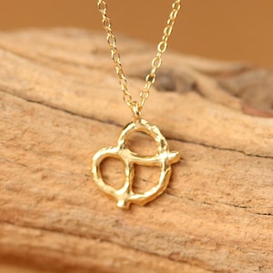 May include: A gold chain necklace with a small, textured pretzel pendant.