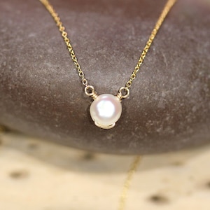 May include: A delicate gold chain necklace with a single white pearl pendant.