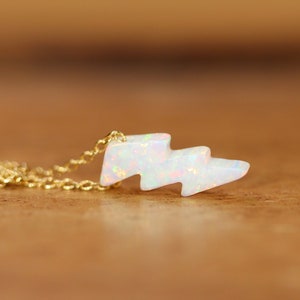 May include: A gold chain necklace with a white opal lightning bolt pendant.