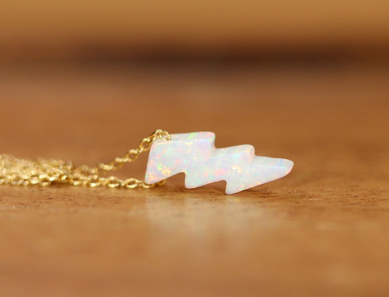 May include: A gold chain necklace with a white opal lightning bolt pendant.