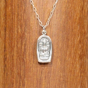 May include: A silver chain necklace with a small silver pendant featuring a detailed image of a seated Buddha.