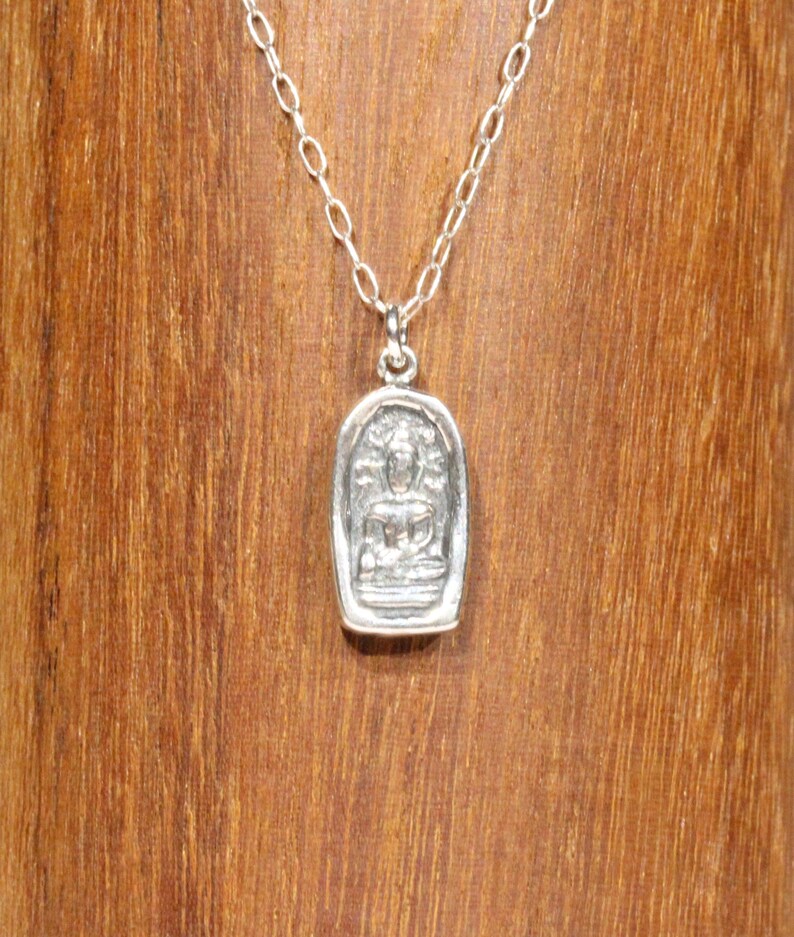May include: A silver chain necklace with a small silver pendant featuring a detailed image of a seated Buddha.