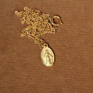K&ouml;nnte beinhalten: Eine goldene Kettenkette mit einem kleinen ovalen Anh&auml;nger, der ein religi&ouml;ses Bild der Jungfrau Maria zeigt.
