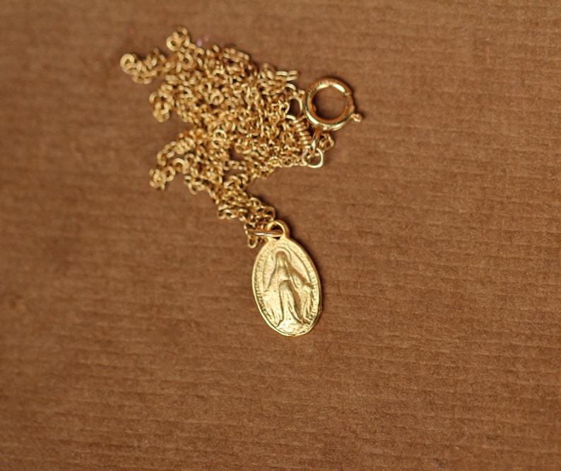 K&ouml;nnte beinhalten: Eine goldene Kettenkette mit einem kleinen ovalen Anh&auml;nger, der ein religi&ouml;ses Bild der Jungfrau Maria zeigt.