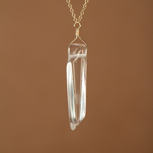May include: A gold chain necklace with a clear quartz crystal pendant. The crystal is faceted and has a pointed tip.