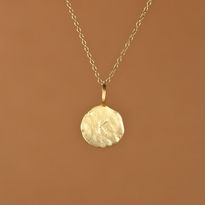 Puede incluir: Un collar de cadena de oro con un colgante redondo con la letra K.
