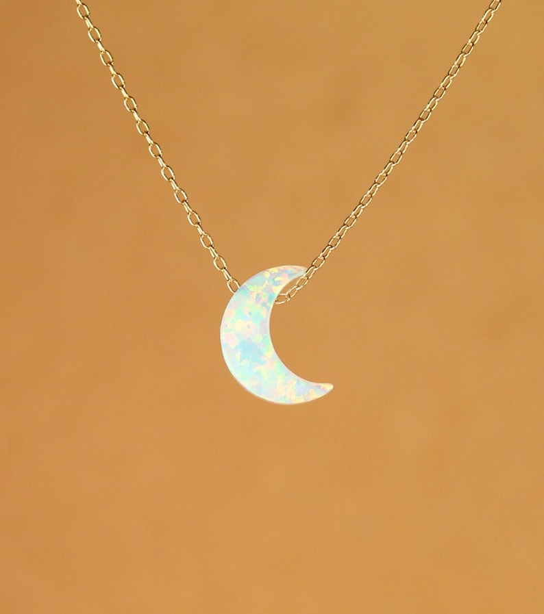 May include: A gold chain necklace with a crescent moon pendant made of iridescent opal.