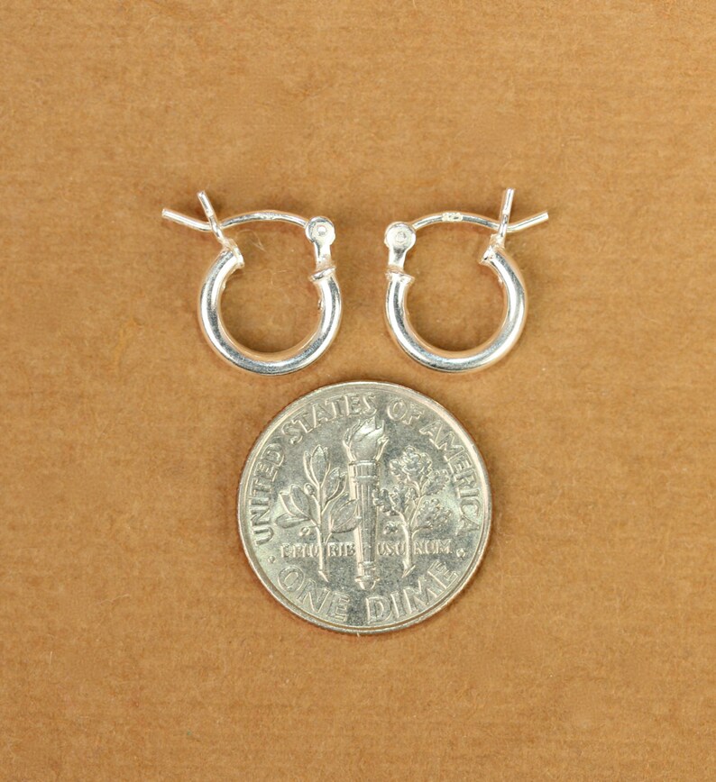 May include: A pair of silver hoop earrings, shown next to a US dime for size comparison.