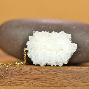 May include: A delicate gold chain necklace with a white crystal cluster pendant. The crystal cluster is a natural formation with a rough, textured surface.
