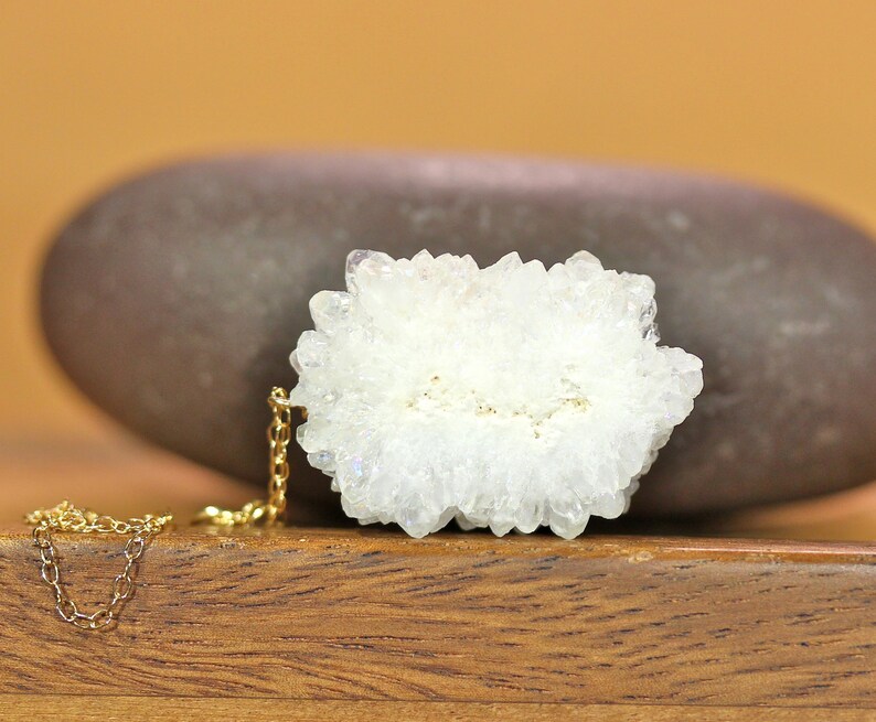 May include: A delicate gold chain necklace with a white crystal cluster pendant. The crystal cluster is a natural formation with a rough, textured surface.