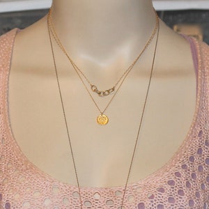 May include: A gold necklace with three chains, one with a small round pendant featuring a sun design. The necklace is worn on a mannequin with a pink crocheted top.