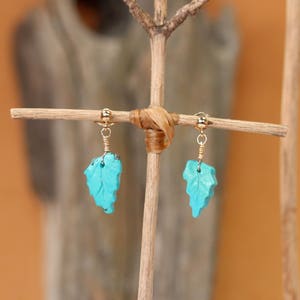 May include: A pair of turquoise leaf earrings with gold wire and a gold bead at the top of each earring.