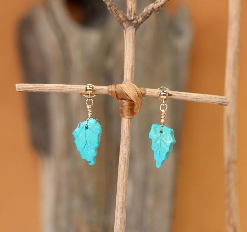 May include: A pair of turquoise leaf earrings with gold wire and a gold bead at the top of each earring.