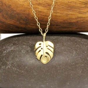 Peut inclure: Un collier en or avec une cha&icirc;ne d&eacute;licate et un pendentif en forme de feuille de monstera.
