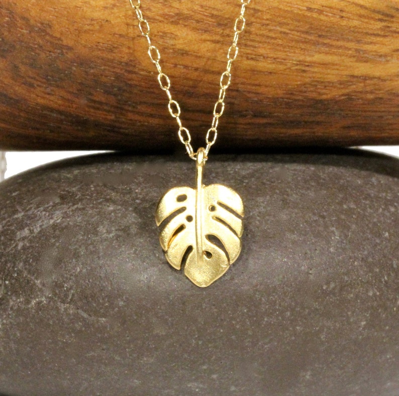 Peut inclure: Un collier en or avec une cha&icirc;ne d&eacute;licate et un pendentif en forme de feuille de monstera.