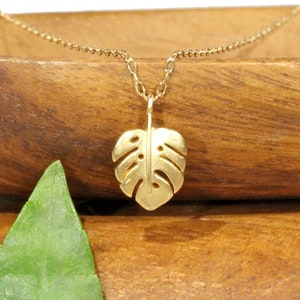 Peut inclure: Un collier en or avec une cha&icirc;ne d&eacute;licate et un pendentif en forme de feuille de monstera.