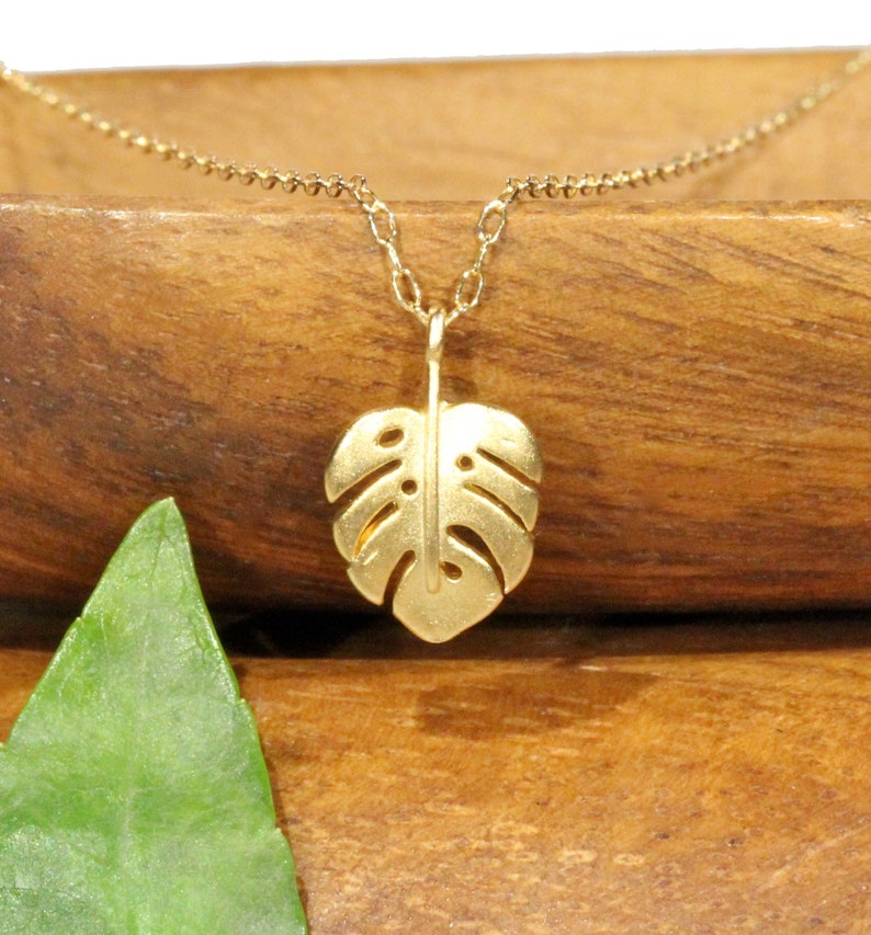 Peut inclure: Un collier en or avec une cha&icirc;ne d&eacute;licate et un pendentif en forme de feuille de monstera.