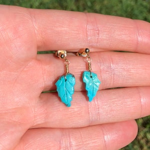 May include: A pair of turquoise leaf earrings with gold wire and posts. The leaves are carved with a detailed design.