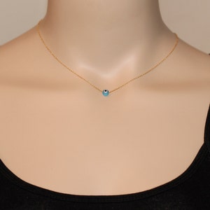 Puede incluir: Un collar de cadena dorada con un peque&ntilde;o dije azul de ojo turco. El collar est&aacute; en un maniqu&iacute; que lleva un top negro sin mangas.