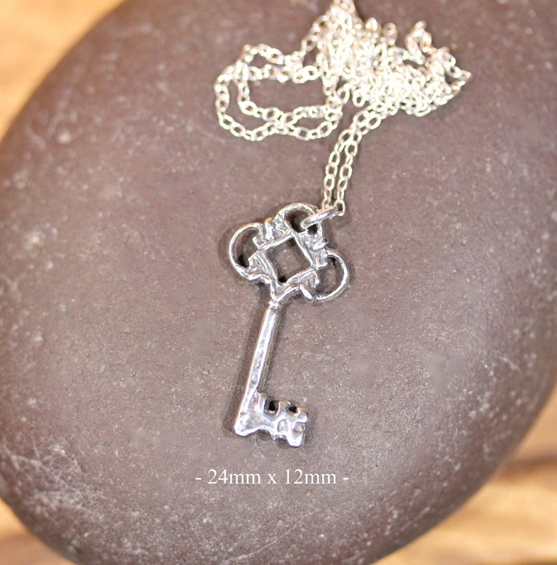 May include: Silver key pendant necklace with a detailed ornate design. The key measures 24mm x 12mm.