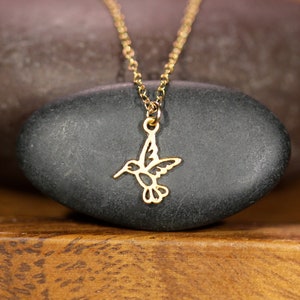 May include: A gold necklace with a delicate hummingbird pendant. The hummingbird is cut out of the metal and has a detailed design.